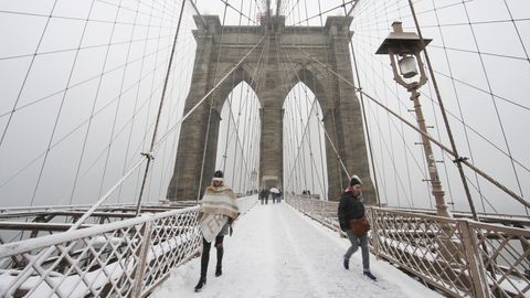 Zwei warm angezogene Menschen gehen im Schnee über die Brooklyn Bridge auf die Kamera zu
