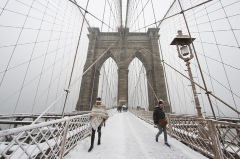 Zwei warm angezogene Menschen gehen im Schnee über die Brooklyn Bridge auf die Kamera zu