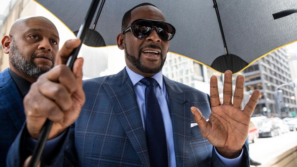 Sänger R. Kelly mit einem Regenschirm und Body Guard an seiner Seite
