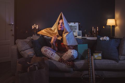 Frau sitzt auf dem Sofa und hat sich verzweifelt Geschenkpapier über den Kopf gezogen