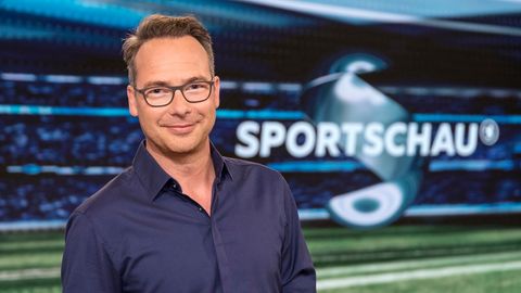 Im dunkelblauen Hemd steht Moderator Matthias Opdenhövel im Fernsehstudio vor dem "Sportschau"-Schriftzug und lächelt