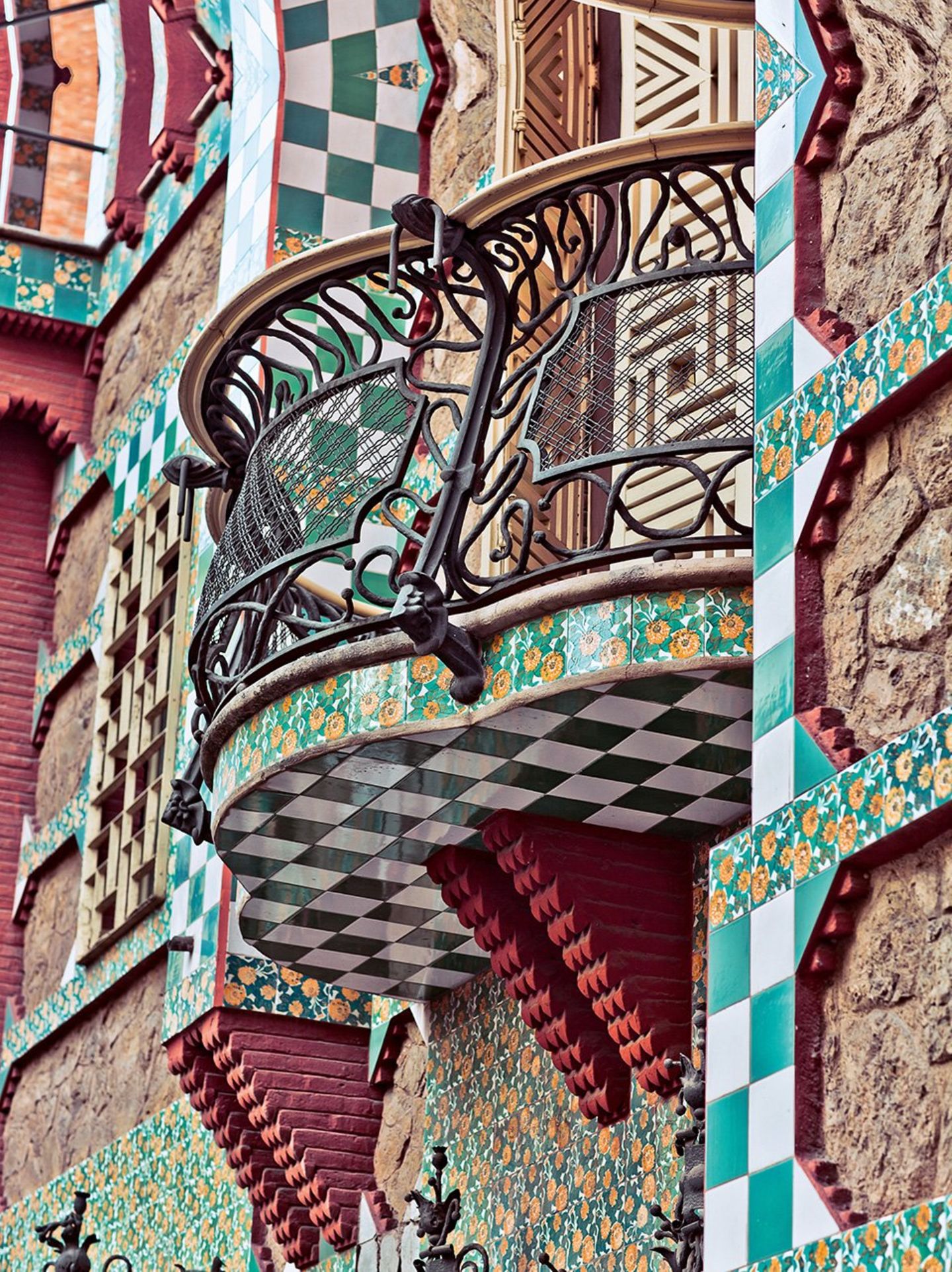 Gaudí Casa Vicens, 1878–1888, Calle de les Carolines, Barcelona. Prunkvoller kann man sich das Debut eines jungen Architekten kaum mehr vorstellen. Wie ein Märchenschloss aus "Tausendundeiner Nacht" erhebt es sich vor dem Besucher der Calle de les Carolines 24 in Barcelona. Und doch ist es in Wirklichkeit ein recht kleines Haus, auch nicht die Heimat eines Prinzen, sondern das Wohnhaus eines Börsenmaklers. Straßenseitiger Balkon im Anbau. Orange-gelbe Nelken füllen die farbigen Fliesen, so wie sie Gaudí auf dem noh leeren Grundstück gesehen haben soll.