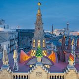 Palacio Güell, 1885_1889, Calle Nou de la Rambla, Barcelona. Wo man sich auch hinstellt in der Calle de la Rambla, es wird schwerfallen, den Palast, den Gaudí für seinen Freund Eusebi Güell erbaute, ganz in den Blick zu bekommen. Das liegt gewiss nicht an seiner Größe: Der Bauplatz ist nur 18 mal 22 Meter groß. Doch die Straße ist so eng, dass man nicht weit genug zurückweichen kann.  Die farbenfrohe Gestaltung der Dachaufsätze mit ihren Trencadís (Mosaike aus unterschiedlich großen Bruchstücken keramischer Fliesen, Marmor oder Glasscherben) macht das flache Dach zu einem stilisierten Wald inmitten der Enge der Altstadt. Um die zentrale Kuppel gruppieren sich Schornsteine und auch Belüftungen für die Ställe im Untergeschoss.