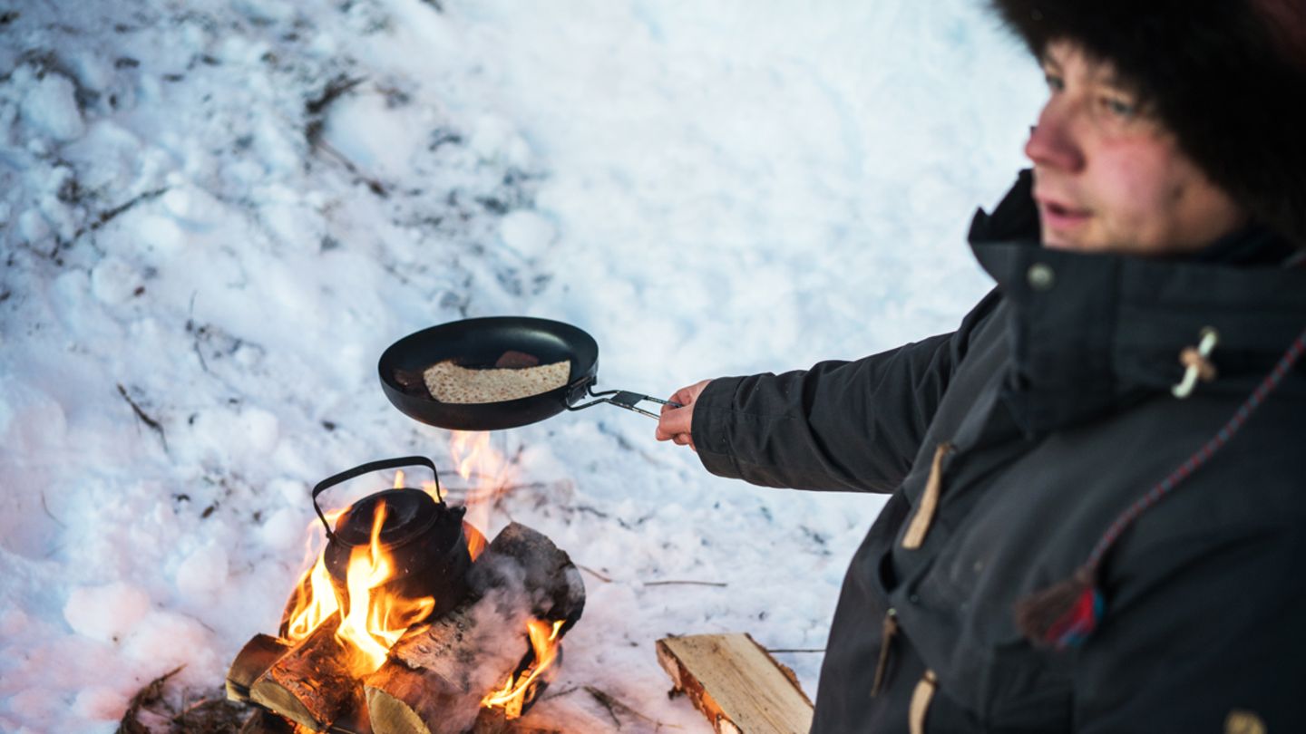 Der Rentierhirte Carl-Johan Utsi macht eine Pause und wärmt Elchfleisch und Brot über offenem Feuer auf, um sich für den langen, kalten Arbeitstag zu stärken
