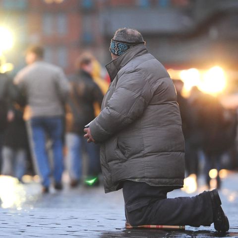 Ein Bettler kniet im Morgengrauen auf dem Fischmarkt am Hafen in Hamburg vor vorbeilaufenden Besuchern