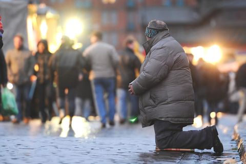 Ein Bettler kniet im Morgengrauen auf dem Fischmarkt am Hafen in Hamburg vor vorbeilaufenden Besuchern