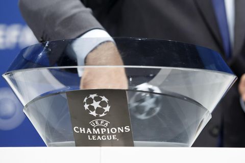 Die Hand eines Mannes im Anzug steckt in einer Glasschale mit "Champions League"-Logo