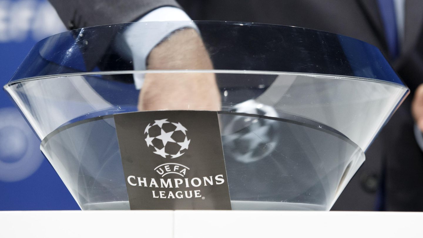 Die Hand eines Mannes im Anzug steckt in einer Glasschale mit "Champions League"-Logo