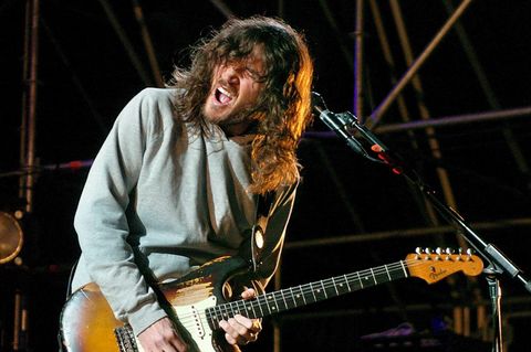 Ein Mann mit langen, braunen Haaren spielt mit offenem Mund und geschlossenen Augen E-Gitarre