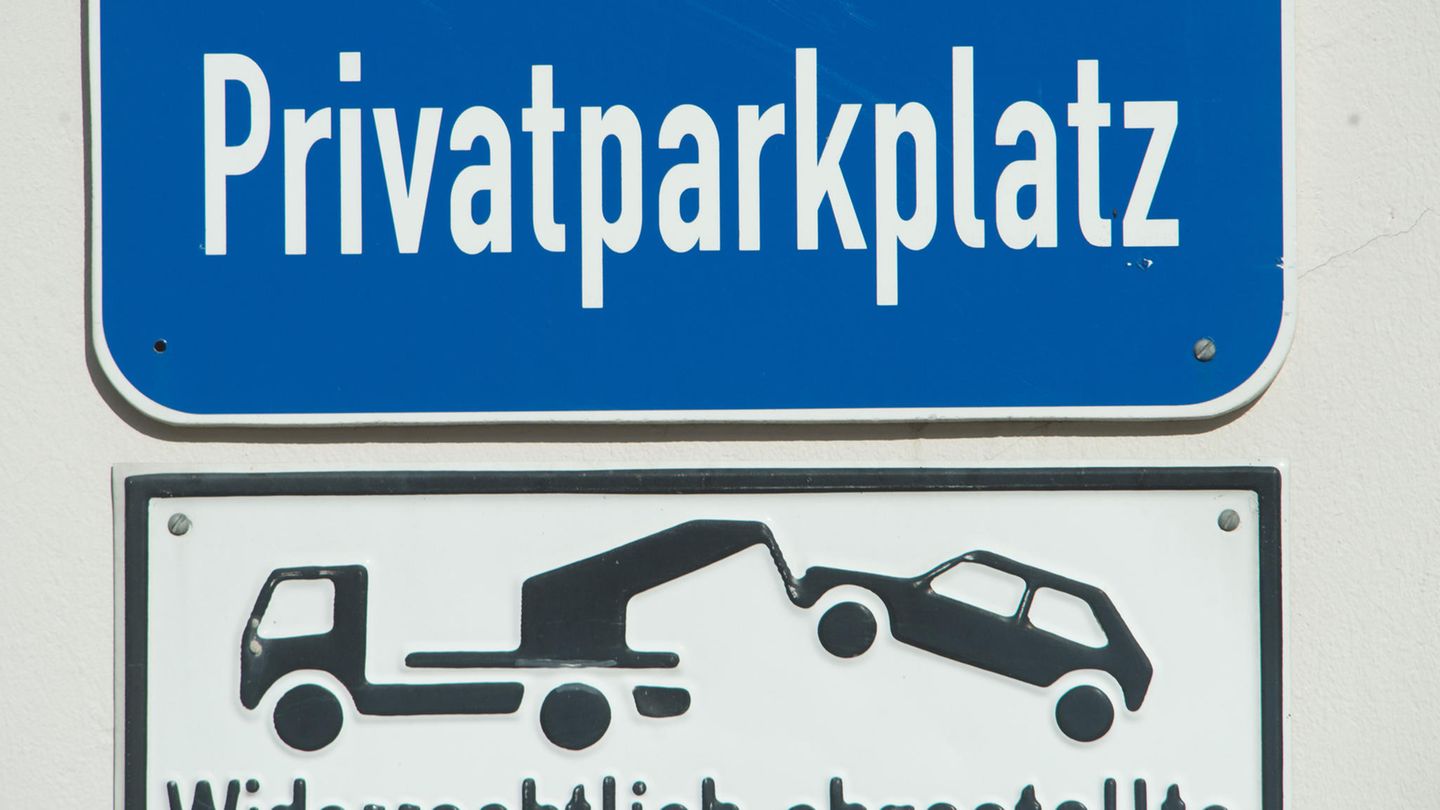 An einer weißen Wand hängt ein blaues Hinweisschild "Privatparkplatz"