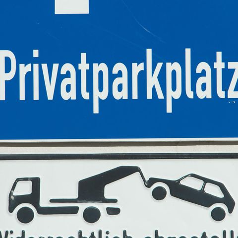 An einer weißen Wand hängt ein blaues Hinweisschild "Privatparkplatz"