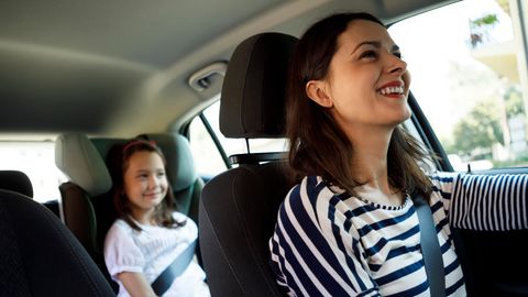 Eine Frau fährt lächelt Auto und sieht im Rückspiegel ihre Tochter an
