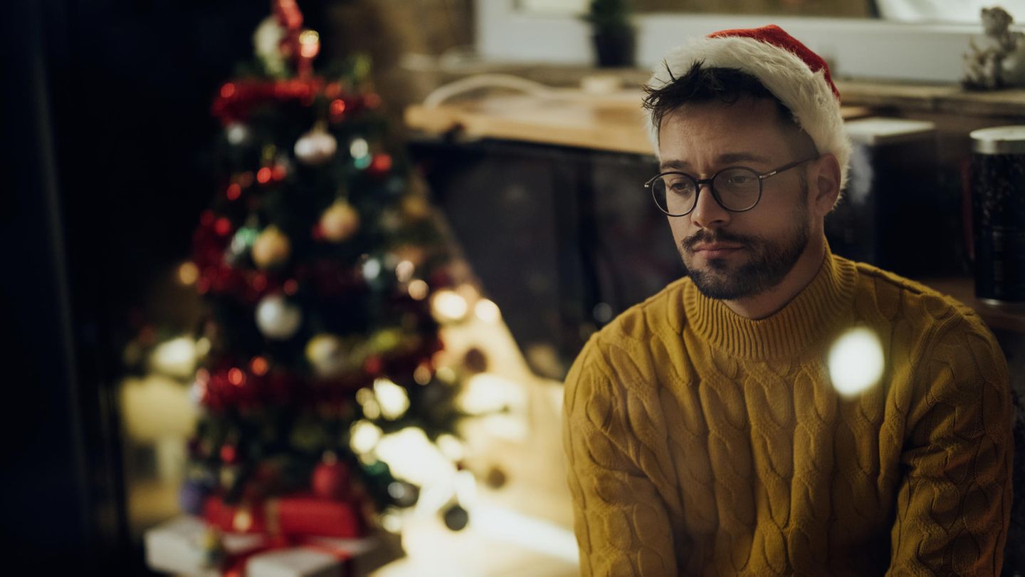 Ein Mann sitzt alleine zu Hause vor einem Weihnachtsbaum