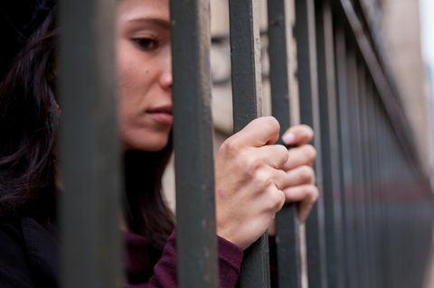 Eine inhaftierte Frau umfasst die Gitterstäbe ihrer Zelle