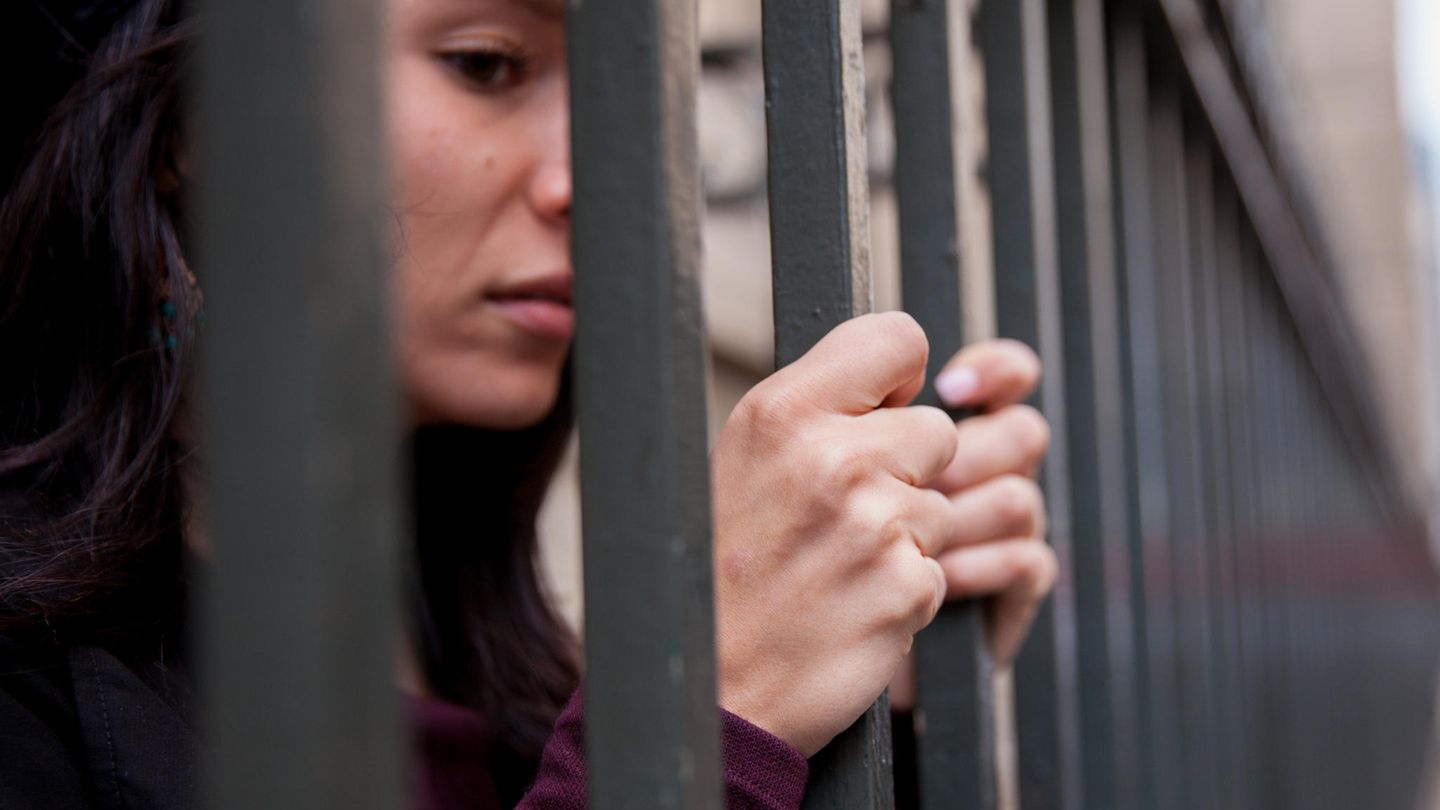 Eine inhaftierte Frau umfasst die Gitterstäbe ihrer Zelle