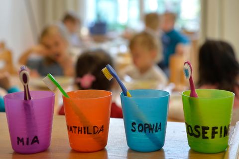 Zahnbürsten und Zahnputzbecher mit den Vornamen der Kinder stehen in einer Kindertagesstätte auf einem Tisch