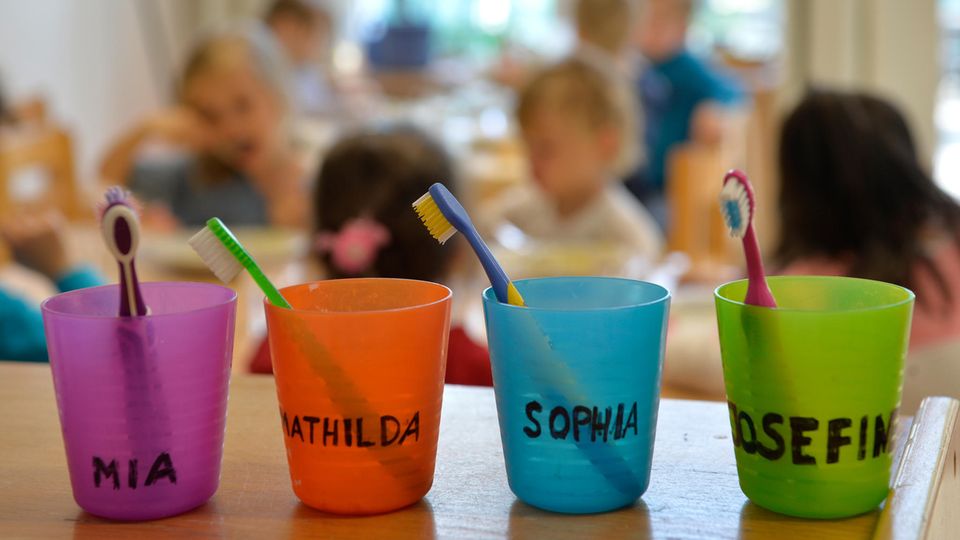 Zahnbürsten und Zahnputzbecher mit den Vornamen der Kinder stehen in einer Kindertagesstätte auf einem Tisch