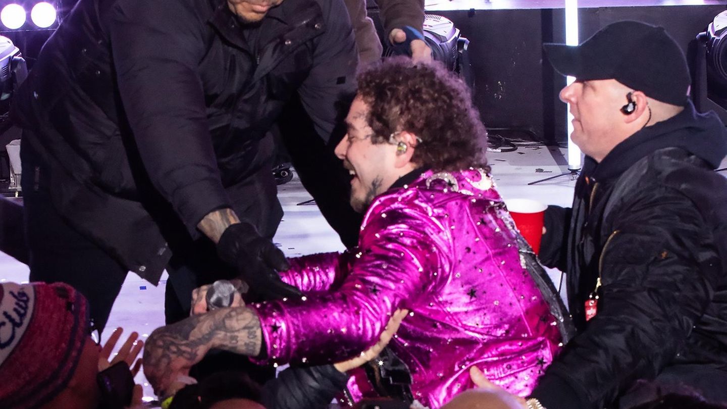 Post Malone im pinken Anzug. Security-Mitarbeiter helfen ihm nach seinem Sturz wieder auf die Bühne