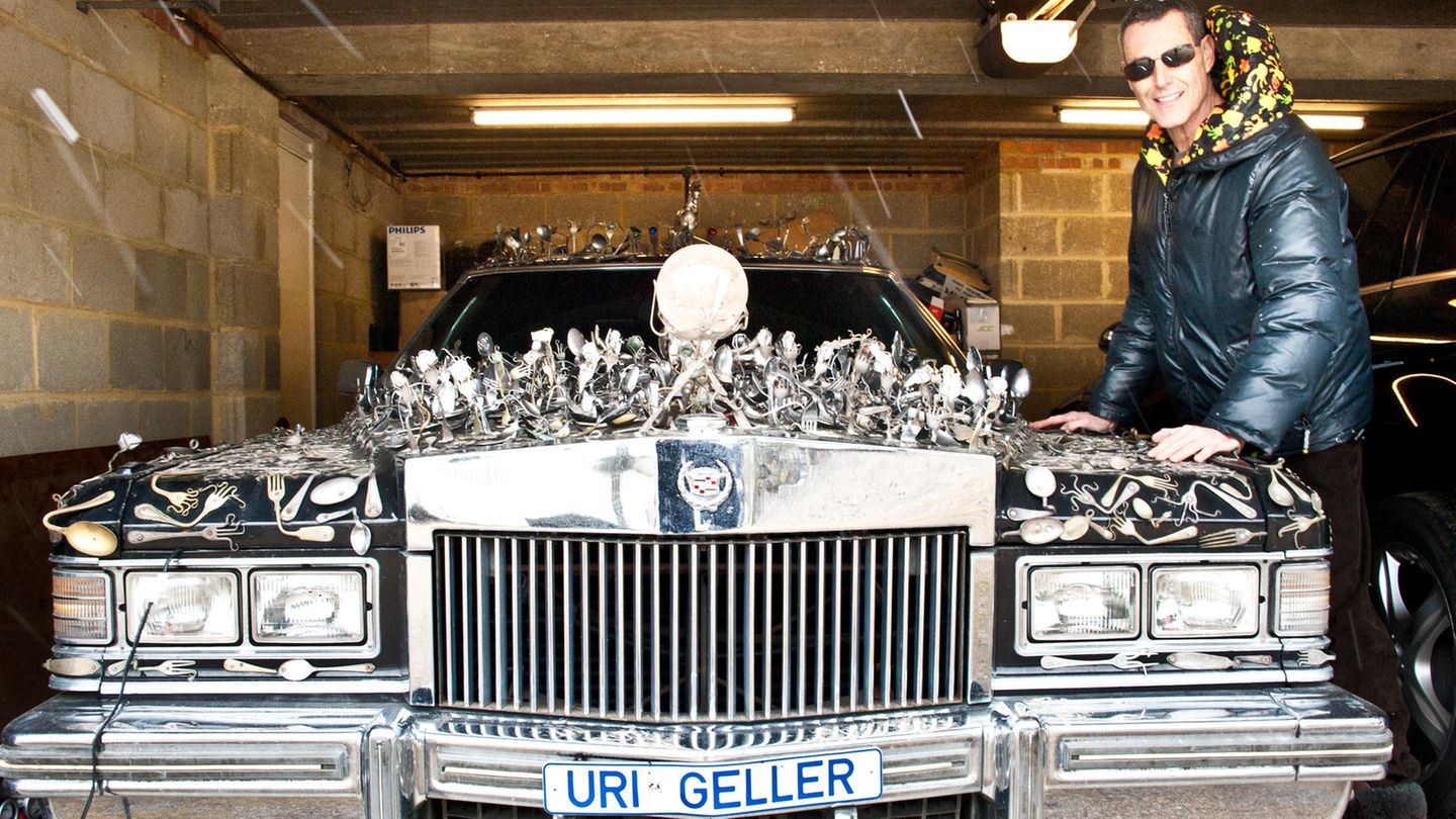 Uri Geller steht neben seinem Cadillac, auf dem Löffel befestigt sind