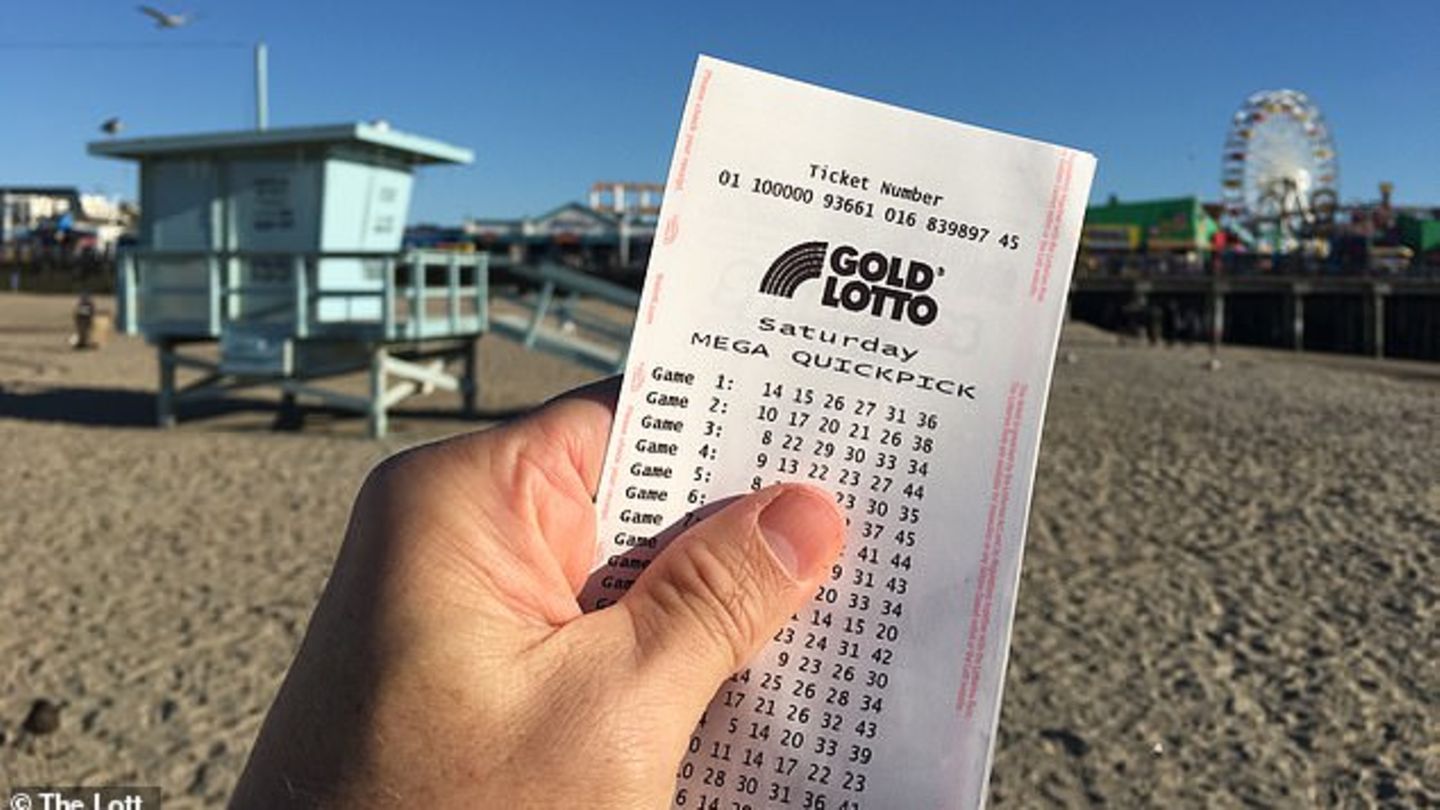 Eine Hand zeigt einen Lottoschein am Strand