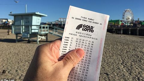 Eine Hand zeigt einen Lottoschein am Strand