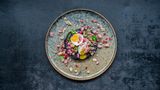 Rotkohlsteak mit Schinken-Granatapfel-Crumble      Für 4 Personen  1 mittelgroßer Rotkohl  Salz  Für den Schinken-Granatapfel-Crumble  2 rote Zwiebeln  2 EL Sonnenblumenöl  200 g geräucherte Schinkenwürfel  1 sehr kleine getrocknete Chilischote  4 EL Granatapfelkerne  Zum Anrichten  4 Eier (Größe M)  4 Stängel Dill  4 Stängel glatte Petersilie  60 g Walnusskerne  Zubereitungszeit 25 Min + 1 h Garzeit      Zubereitung  • Den Backofen auf 250°C (Umluft) vorheizen. Den Rotkohl waschen, trocken tupfen und auf den Rost in den Ofen legen. Ein Backblech darunter schieben, da der Kohl beim Garen tropft. Kohl im Ofen 1–1 ½ Stunden verbrennen lassen. Eine Garprobe (zum Beispiel mit einer Messerspitze) machen, der Kohl sollte weder weich noch zu fest sein.  • Inzwischen für den Schinken-Crumble die Zwiebeln abziehen und fein würfeln. Das Öl in einer Pfanne erhitzen und die Zwiebelwürfel darin bei mittlerer Hitze etwa 4 Minuten anschwitzen, dabei öfter umrühren. Die Schinkenwürfel dazugeben und alles weitere 2–3 Minuten braten. Die Chilischote zerbröseln, untermengen und die Pfanne vom Herd nehmen. Die Granatapfelkerne unter den leicht abgekühlten Zwiebel-Schinken-Mix heben.  • Die Eier in kochendem Wasser in 6 Minuten wachsweich kochen. Abschrecken und pellen.  • Dill und Petersilie waschen, trocken schütteln und die Spitzen beziehungsweise Blätter abzupfen. Die Walnusskerne grob hacken und in einer Pfanne ohne Fett bei mittlerer Hitze unter Rühren rösten, bis sie duften. Auf einem Teller abkühlen lassen.  • Den Rotkohl aus dem Ofen nehmen, die äußeren, dunklen Blätter entfernen und den Kohl in 1,5 – 2 cm dicke Scheiben ("Steaks") schneiden. Je ein Steak pro Teller anrichten, leicht mit Salz würzen und 2–3 EL Crumble daraufgeben. Eier halbieren, mit etwas Salz bestreuen und jeweils zwei Hälften auf den Teller legen. Mit Kräutern und Walnusskernen bestreut servieren.      Nährwerte pro Portion: Kcal 467 | E 26 g | F 31 g | KH 14 g
