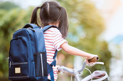 Ein Mädchen mit Zöfen und Rucksack sitzt auf einem Fahrrad