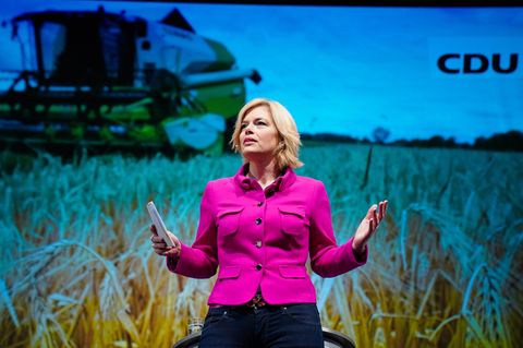 Julia Klöckner auf dem Landesparteitag der CDU. Hinter ihr ist ein Feld mit einem landwirtschaftlichen Fahrzeug zu sehen.