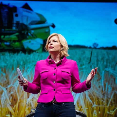 Julia Klöckner auf dem Landesparteitag der CDU. Hinter ihr ist ein Feld mit einem landwirtschaftlichen Fahrzeug zu sehen.