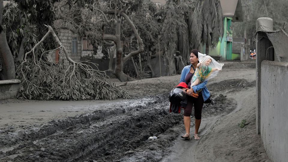 Der Vulkan Taal auf den Philippinen hat die Landschaft unter einen Grauschleier gelegt, die Menschen flüchten. Eine Frau trägt in dem Ort Boso-Boso eine Statue des Jesuskindes in Sicherheit.