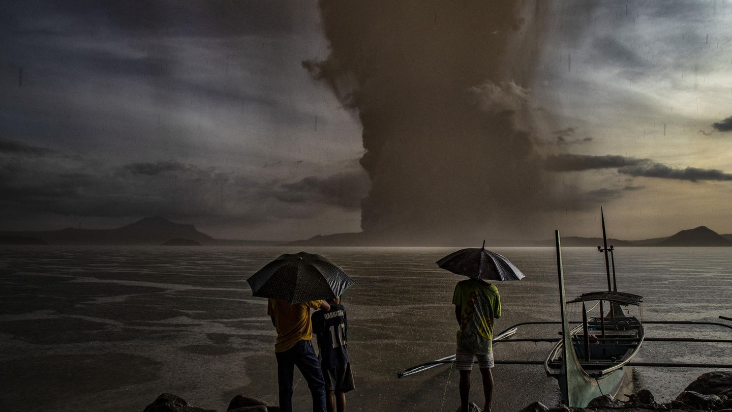 Der Ausbruch verdunkelte phasenweise den Himmel. Diese Menschen wagen dennoch geschützt unter Regenschirmen einen Blick auf den Taal.