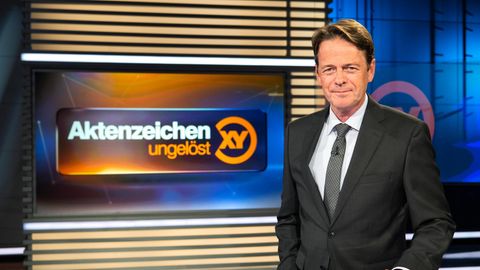 Moderator Rudi Cerne mit dem Logo der Sendung Aktenzeichen XY"