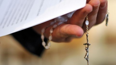 Ein Priester hält einen Rosenkranz und Dokumente in der Hand
