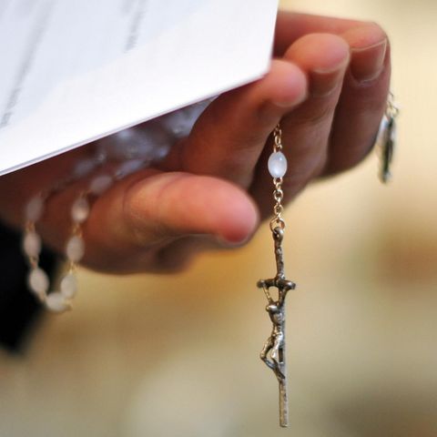 Ein Priester hält einen Rosenkranz und Dokumente in der Hand