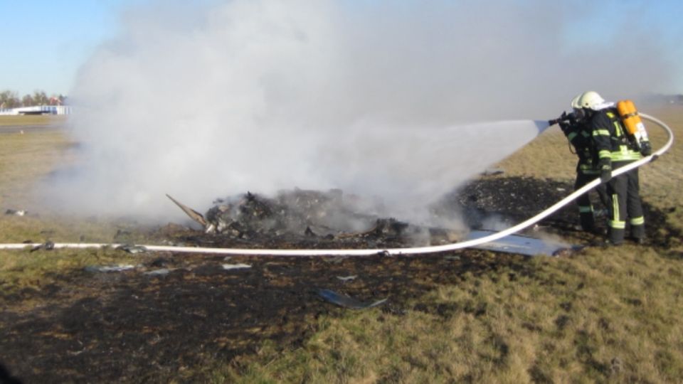 Kleinflugzeug Absturz Strausberg Zwei Feuerwehrleute löschen auf einer verkohlten Wiese die Trümmer eines abgestürzten Kleinflugzeugs