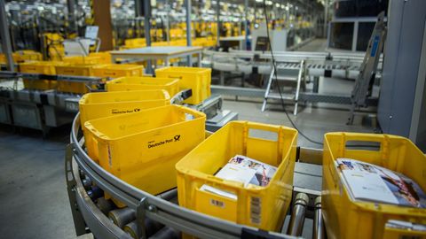Gelbe Kisten zum Sortieren von Briefen laufen im Briefzentrum Kiel der Deutschen Post über ein Förderband