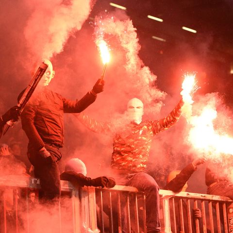 Auf einem Metallzaun im Millerntorstadion sitzen Vermummte und brennen Signalfackeln ab