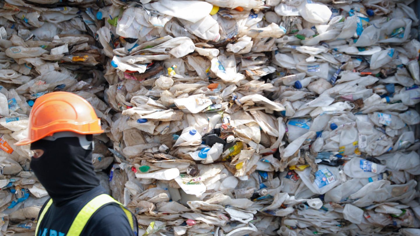Ein Arbeiter vor einem Berg zerdrückter Plastikflaschen