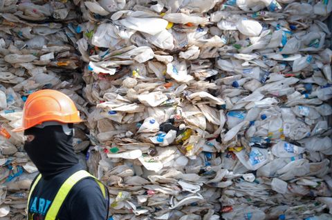 Ein Arbeiter vor einem Berg zerdrückter Plastikflaschen