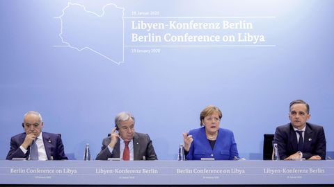 Auf einem Podium mit Bundesadler sitzen drei Männer in Anzügen und Bundeskanzlerin Angela Merkel. Sie trägt einen blauen Blazer