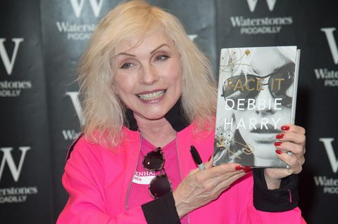 Debbie Harry hält ihre Autobiografie in die Kamera und lächelt