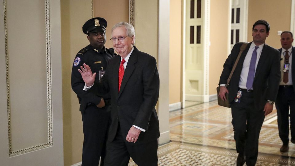Mitch McConnell, ein weißhaariger Mann mit schwarzem Anzug und roter Krawatte, verlässt den Senat und winkt dabei