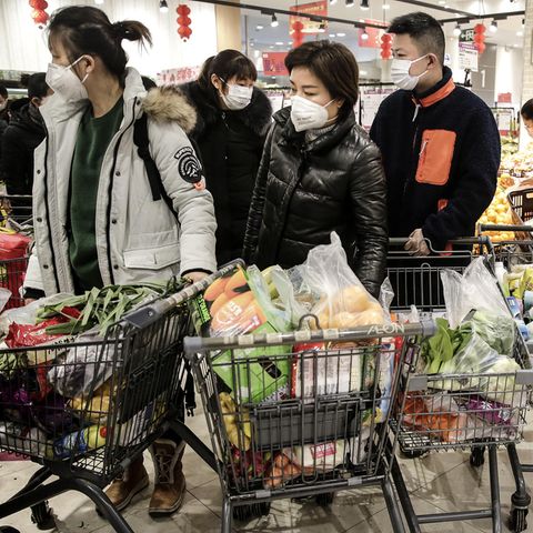 Chinesische Männer und Frauen schieben mit Masken vor dem Mund volle Einkaufswagen mit Lebensmitteln durch einen Supermarkt