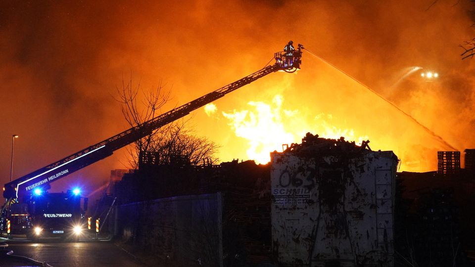 Ilsfeld: Feuerwehrleute versuchen Stapel von brennenden Holzpaletten zu löschen