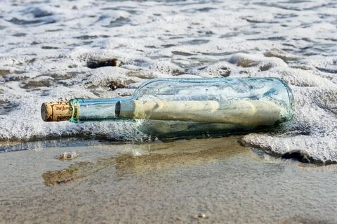 Eine durchsichtige Weinflasche mit einem aufgerollten Papier darin und einem Korken Treibt im Wellensaum