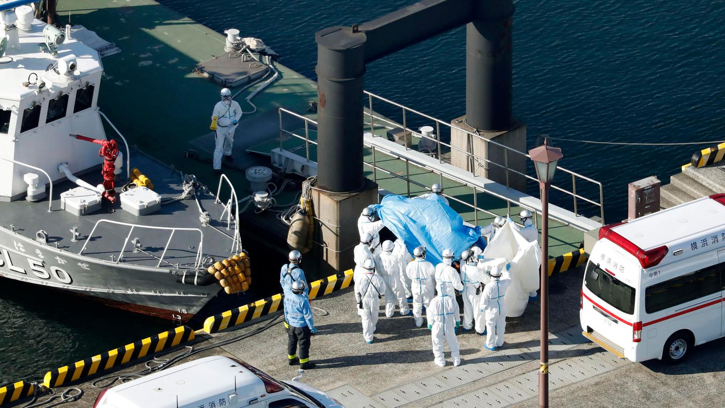 Medizinisches Personal in Schutzanzügen begleitet im Hafen von Yokohama einen Passagier