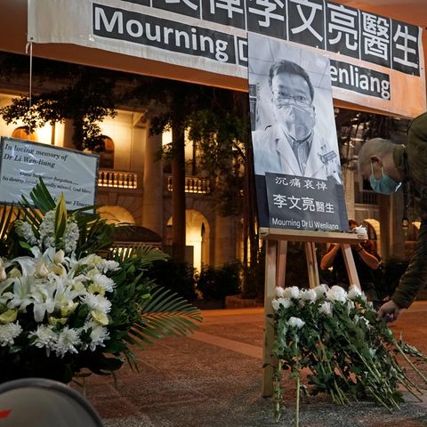 Ein Mann mit einem Mundschutz legt in Hongkong Blumen vor einem Bild Li Wenliangs nieder