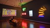 Video- und Neonkunst im Ian Potter Centre in Melbourne: In der Mitte oben ein grünes Neon-Emu auf dem Union Jack: "dhalaay yuulay - passionate skin" und rechts die gelben Neon-Schlagstöcke "Buuga-Buuga", beides Installationen von Brook Andrew.