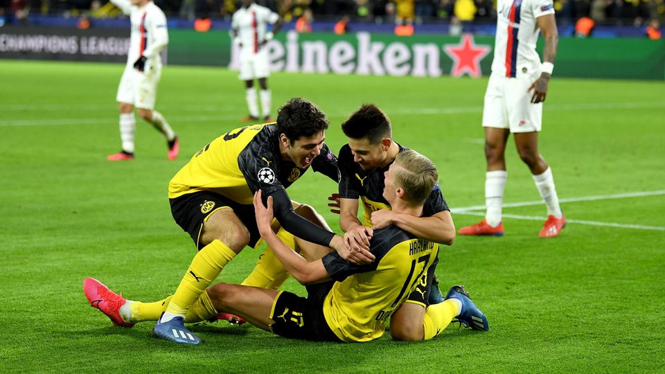 Drei Dortmunder Spieler jubeln auf den Rasen, während PSG-Spieler konsterniert im Hintergrund stehen