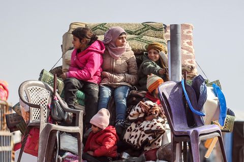 Kinder sitzen auf der Ladefläche eines Kleintransporters auf den Habseligkeiten ihrer Familie